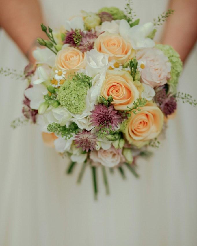 Bride holding a bouquet of peach roses, white freesia and astrantia ready for wedding flower preservation